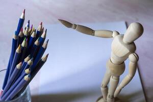 Colored pencils, empty paper and dummy for drawing on the table. photo