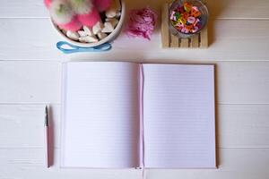 A notepad with pen, pink cactus, crumpled sheet of paper and multicolored letters on a white wooden desktop. photo