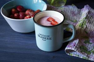 Strawberry dessert. A mug with strawberry creamy fresh, bowl with ripe strawberries and lupine on a dark blue wooden table. Beautiful food still life. photo