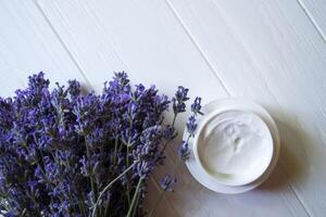 Lavender flowers, candles and cream on a white wooden background. Beauty care. Top view. photo