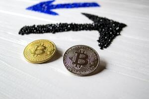 Golden and silver bitcoins with arrows up and down on a white wooden background. photo