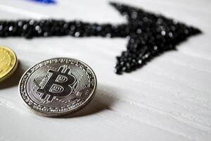 Silver bitcoin with black arrow up on a white wooden background. photo