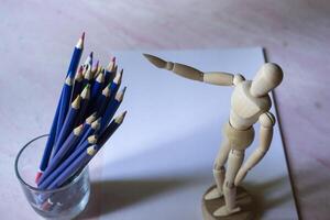 Colored pencils, empty paper and dummy for drawing on the table. photo