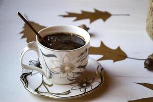 A cup of coffee on a white wooden table, and decoration by oak autumn leaves. photo