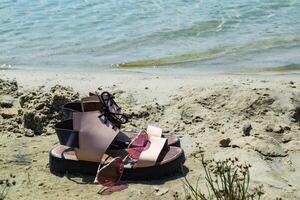 Female shoes and pink glasses on the coast of blue lake. photo