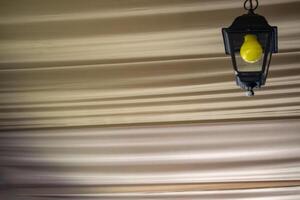 The yellow bulb in the black lantern on the ceiling. Close up. photo