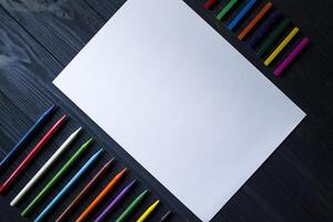 Palette of multicolored pencils and the sheet of white paper on dark blue wooden desk. photo