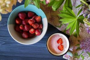 Strawberry dessert. A mug with strawberry creamy fresh, bowl with ripe strawberries and lupine on a dark blue wooden table. Beautiful food still life. photo