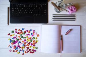 un tableta, computadora portátil, lapices y multicolor letras en un blanco de madera escritorio. escritorio parte superior vista. foto