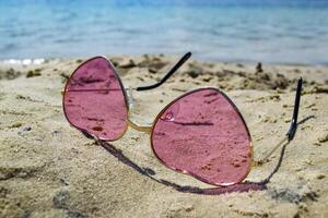 Pink glasses on the sand near blue water of lake. photo