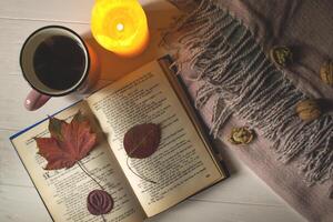 A cup of tea near book and woolen blanket with decoration by fallen leaves. Cozy autumn. photo