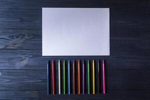 Palette of multicolored pencils and the sheet of white paper on dark blue wooden desk. photo