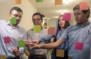 Diverse team of young people in office looking at sticky notes on glass brainstorming photo