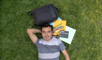 A male student lying on the grass with a backpack and school supplies photo