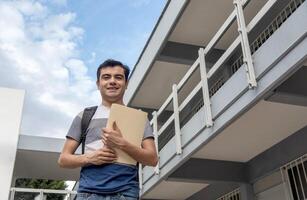 Smiling student holding a paper in front of a school building photo