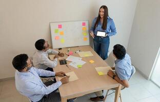 un mujer en pie en frente de un grupo de personas alrededor un mesa foto