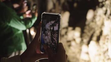 un' ragazza prende immagini di stalagmiti su il parete nel un' grotta su sua Telefono video