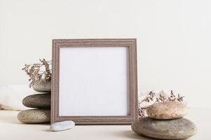 Square empty photo frame near a stack of stones with dried flowers on a light background