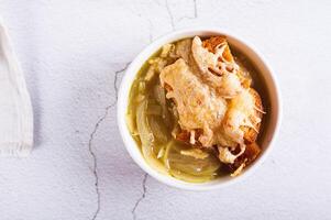 Close up of homemade onion soup with croutons and cheese in a bowl on the table top view photo