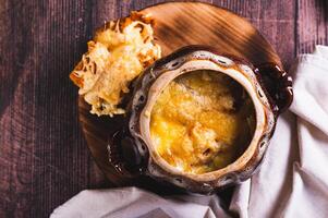 Close up of french onion soup with melted cheese and croutons in a pot on the table top view photo