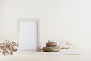 Empty photo frame, dried flowers and stones on a light background