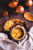 Homemade onion soup with cheese croutons in a pot on the table top and vertical view photo