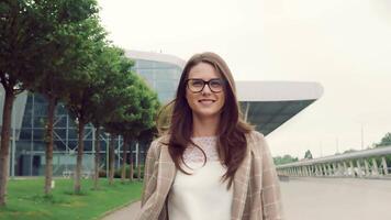 Portrait of a pretty caucasian woman walking with smiling and looking at the camera. Girl on the street on a background of modern interiors smiling at the camera. video