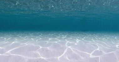 Blue ocean underwater with white sandy bottom and waves. Sea texture video