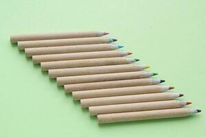 Multi colored pencils isolated on green background. Back to school concept. Sketching and drawing hobby. Stationery supply store. Education process. Top view. Minimal style composition photo