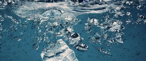 Water splashing and ice cube. Ice splashing into a glass of water. Underwater pouring ice cubes falling into clear watering background. Refreshing chill drinking. Ices in a glass with blue background photo