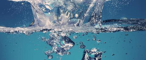 agua salpicaduras y hielo cubo. hielo salpicaduras dentro un vaso de agua. submarino torrencial hielo cubitos que cae dentro claro riego antecedentes. refrescante frío Bebiendo. helados en un vaso con azul antecedentes foto