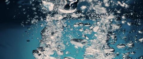 Water splashing and ice cube. Ice splashing into a glass of water. Underwater pouring ice cubes falling into clear watering background. Refreshing chill drinking. Ices in a glass with blue background photo