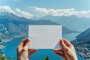 ai generado mujeres manos participación un blanco blanco tarjeta, en contra el fondo de un verano panorámico paisaje con lago, montañas y soleado azul cielo. foto