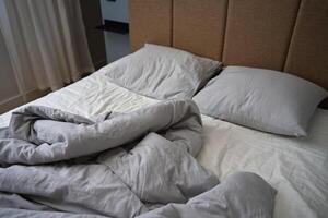 Crumpled bed with pillows, blanket and crumpled sheets in bedroom photo