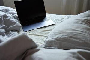 Unmade bed with pillows and crumpled bedsheets and open laptop photo