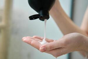 Woman pouring shampoo on hand in bathroom photo