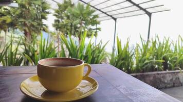 geel keramisch koffie kop Aan een cafe tafel, bokeh achtergrond van groen bomen zwaaiend in de wind video