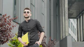 Young male businessman holding a yellow folder with documents and a smartphone. A man reads a message on a smartphone. video