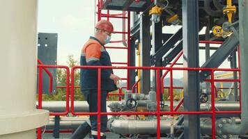 Gasman in a protective mask walking along the gas station and inspecting it. The gas production worker inspects the metal structures of the gas distribution complex. video