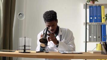 joven africano americano científico mirando mediante un microscopio en un laboratorio video