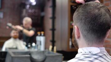 un Barbero en un barbería lo hace pelo peinado para un cliente. ver en el espejo video