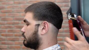 uma jovem cara pega uma corte de cabelo dentro uma barbearia. caucasiano homem video
