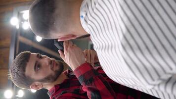 The young barber very carefully cuts the client with a trimmer. Vertical video