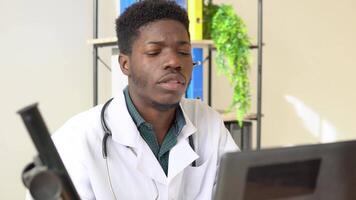 joven africano americano masculino médico con auriculares teniendo charla o consulta en ordenador portátil video