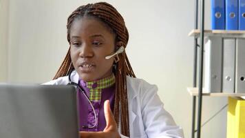 Young african american woman doctor with headset having chat or consultation on laptop video