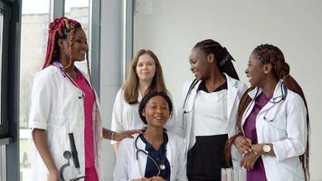 A group of young medics of different races sitting and standing at a table are having a conversation video