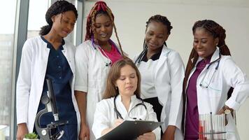 Young doctors of different races have a discussion standing at a table while one of them makes notes video