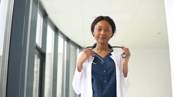 joven africano mujer médico o enfermero en pie en médico traje a clínica y mirando a cámara video