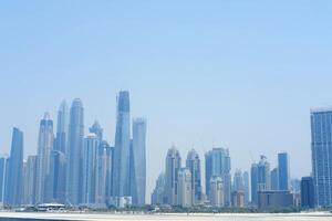 Skyscrapers dominate Dubai's financial district skyline with construction cranes indicating ongoing development. Dubai, UAE - August 15, 2023 photo