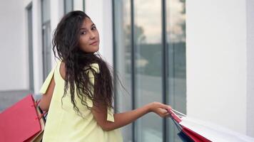 Beautiful girl model in a long yellow dress after shopping with colored bags in hands having a good mood. slow motion. Portrait video